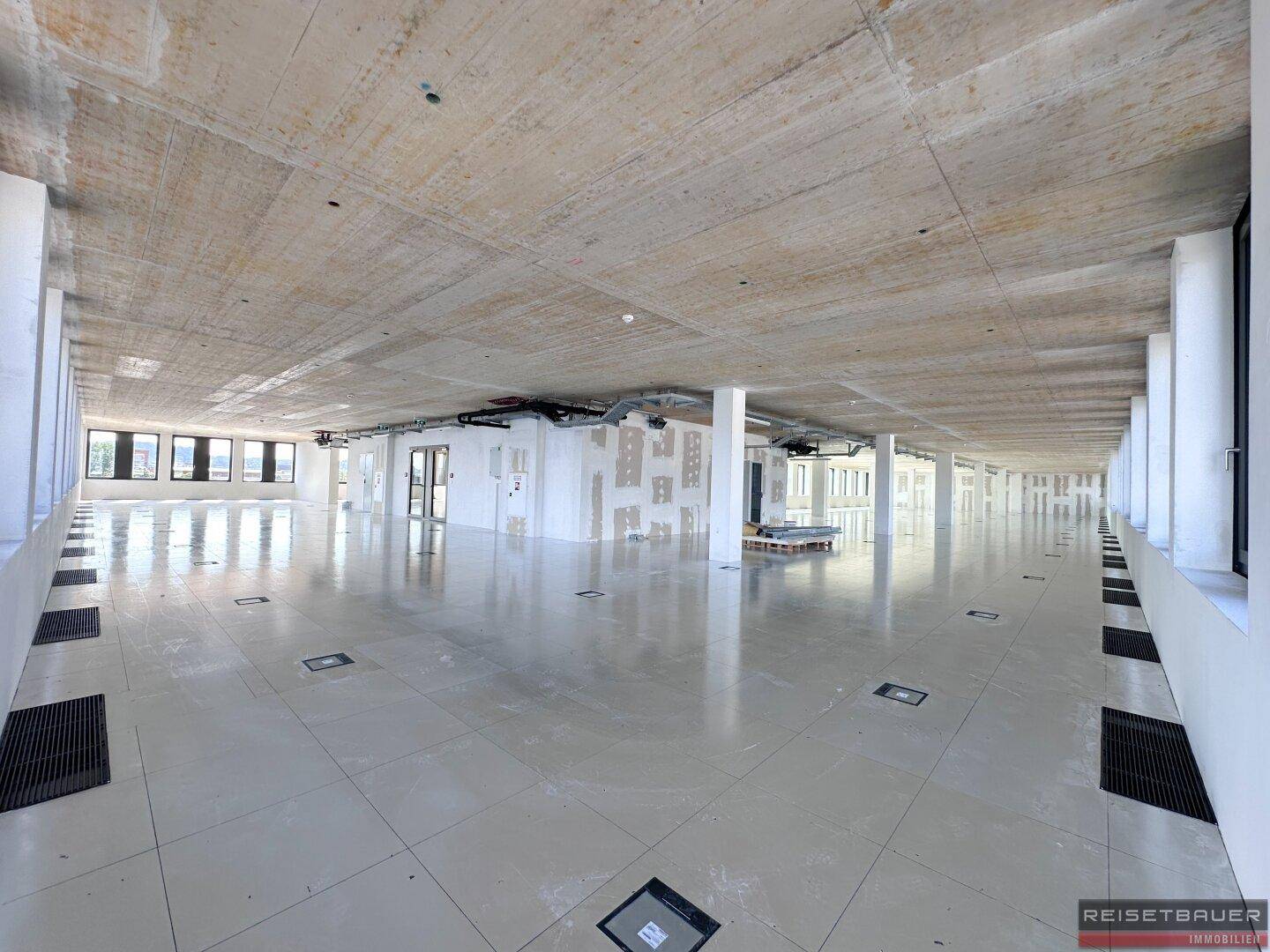 Weitläufiger Bürobereich im Rohzustand mit vielen Fenstern und Blick auf die Umgebung, ideal für flexible Gestaltung.