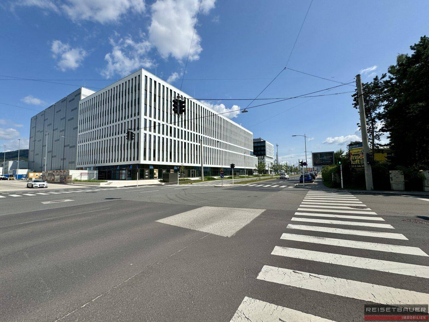 Moderne Bürokomplexe mit markanter weißer Fassade und großen Fensterfronten an einer Kreuzung unter blauem Himmel.