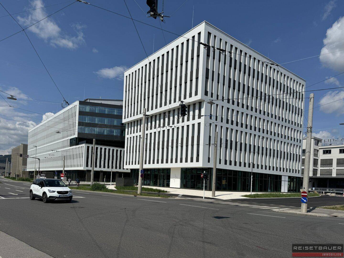 Eckansicht eines modernen Bürokomplexes mit weißer Fassade und vertikalen Fensterbändern an einer belebten Kreuzung.