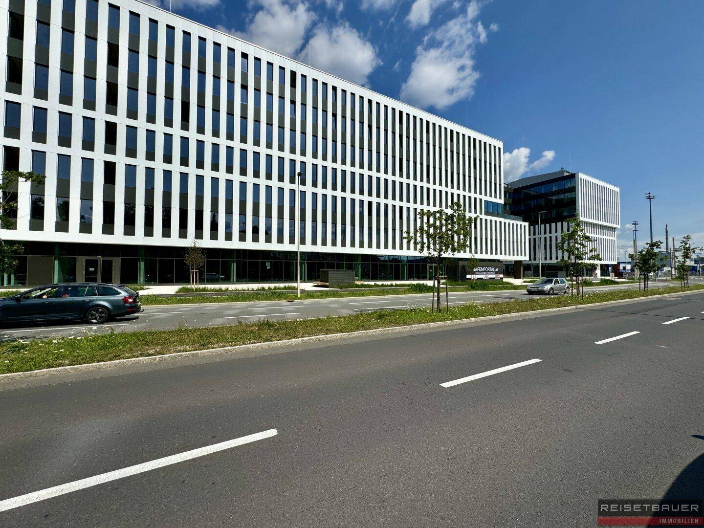Seitenansicht des modernen Bürogebäudes entlang einer Straße, gekennzeichnet durch seine weiße Fassade und großen Fensterfronten.