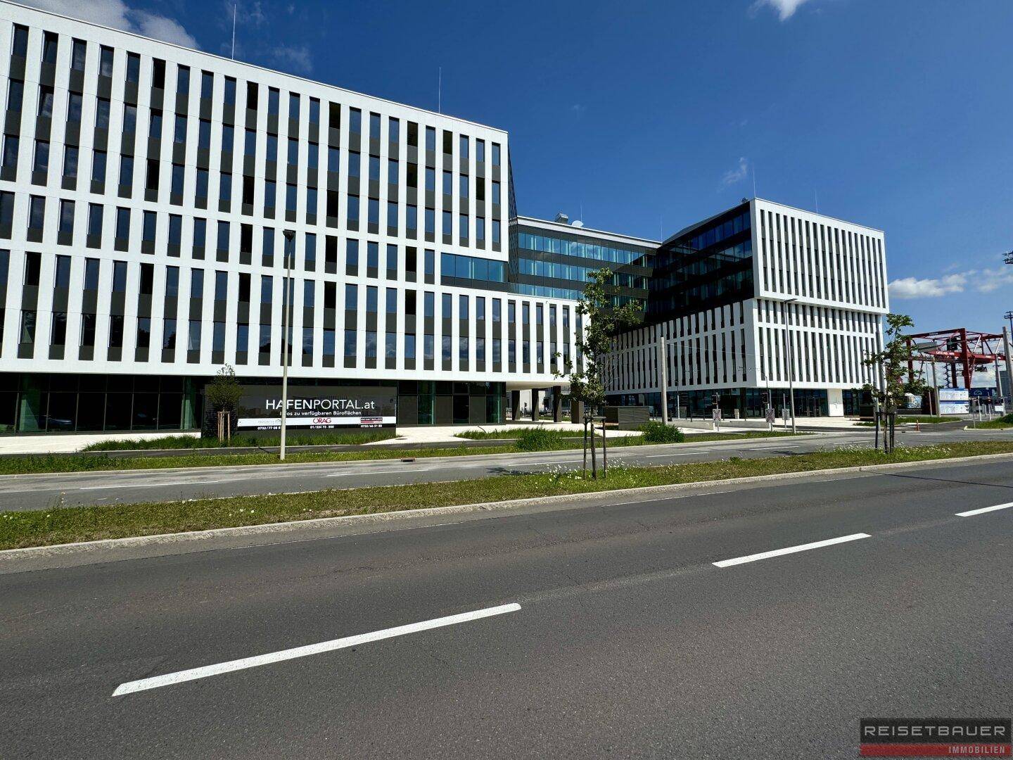 Nahaufnahme der modernen Bürogebäude-Fassade mit dem Schriftzug 'HAFENPORTAL.at' und blauer Himmel.