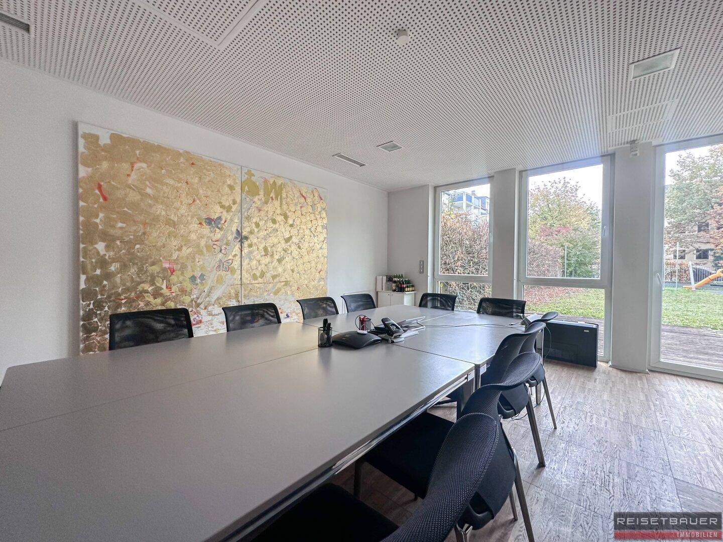 Großer Konferenzraum mit langem Tisch, vielen Stühlen, Kunstwerk und Zugang zum Außenbereich.