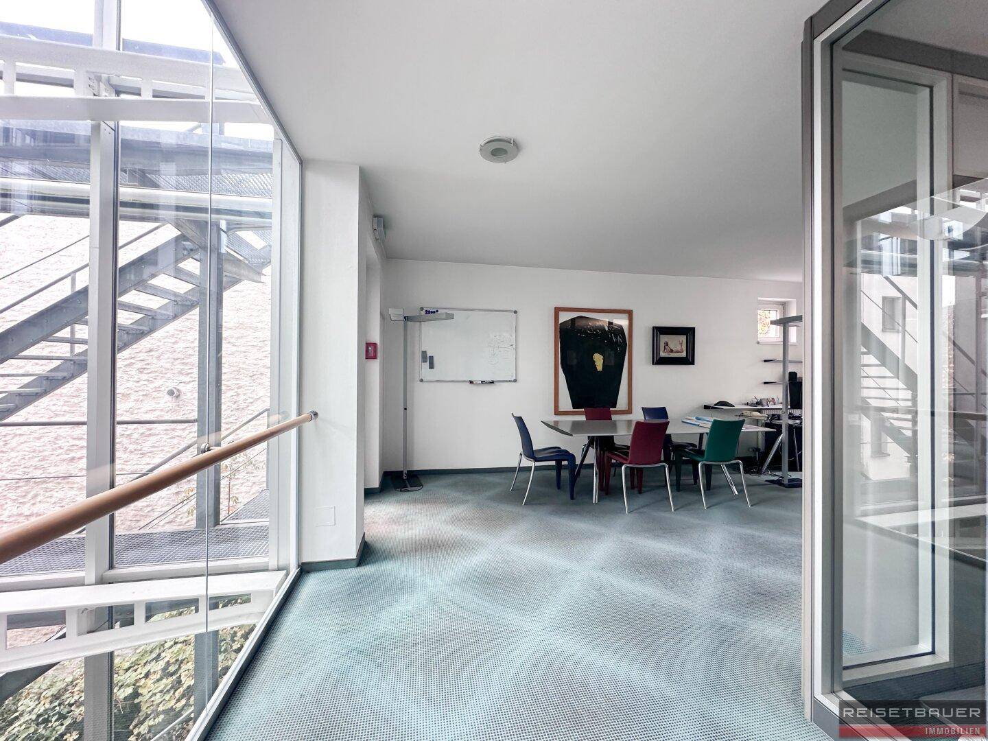 Heller Bürobereich mit Teppichboden, Besprechungstisch und Blick auf den Innenhof.