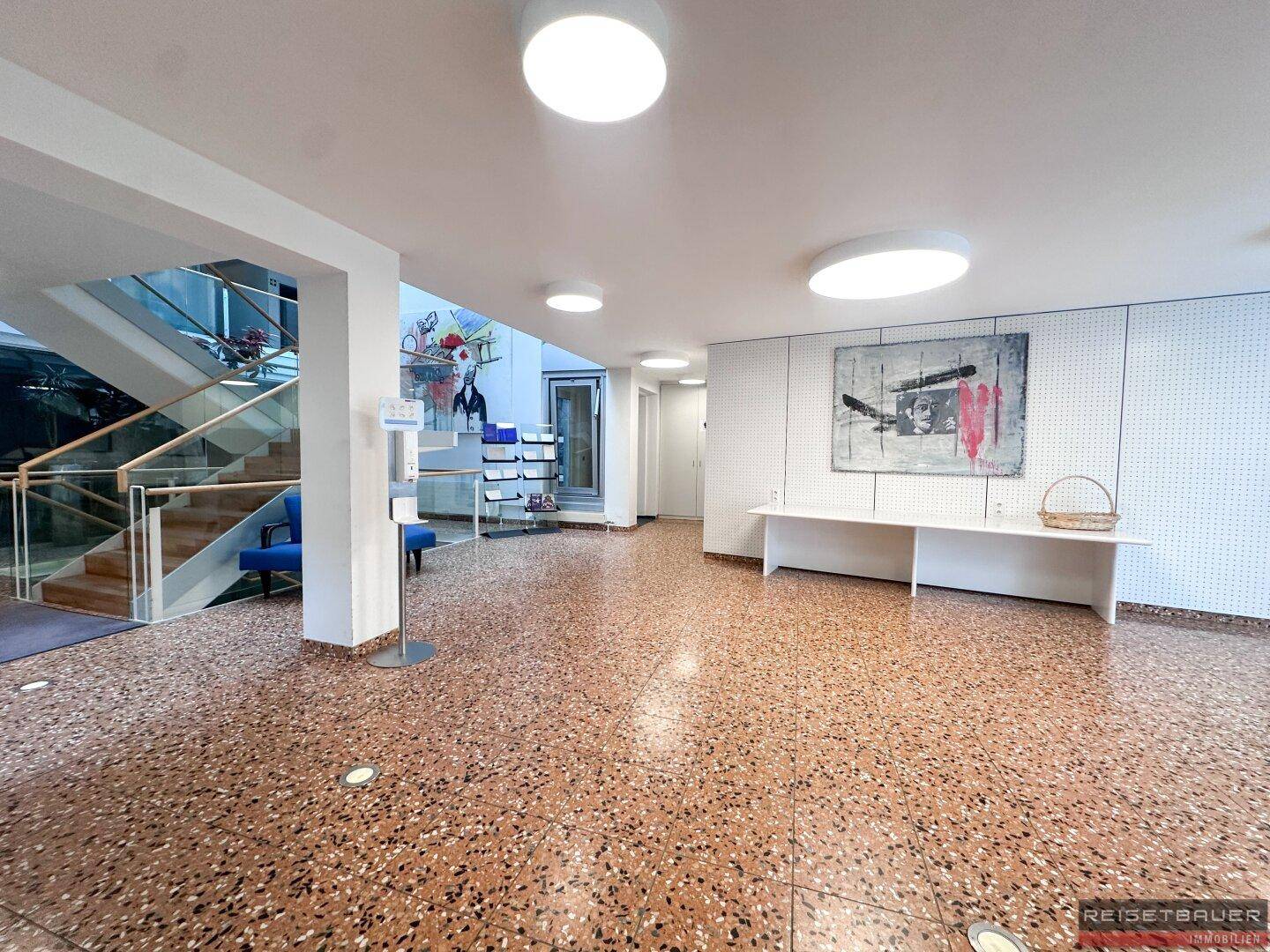 Empfangsbereich mit Terrazzoboden, moderner Kunst und Zugang zu einer Treppe.