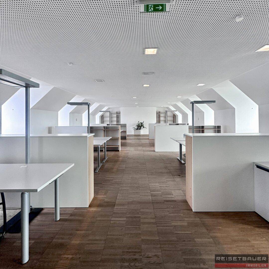 Helles und modernes Großraumbüro mit schrägen Decken, Holzboden und funktionalen Arbeitsbereichen.