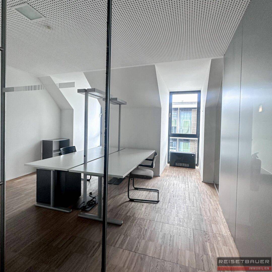 Moderner Arbeitsbereich im Büro mit großem Fenster, Holzboden und viel natürlichem Licht.