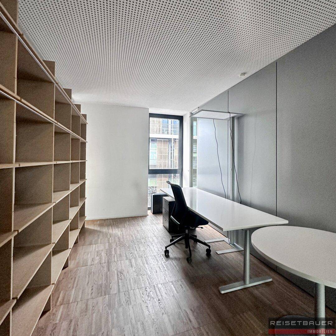 Einzelbüro mit großem Schreibtisch, ergonomischem Stuhl und raumhohen Regalen.