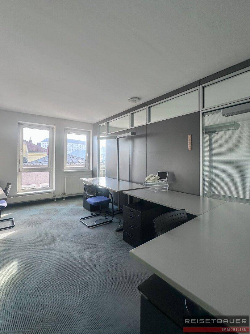Helles Büro mit Teppichboden, modularen Arbeitsplätzen und großen Fenstern.