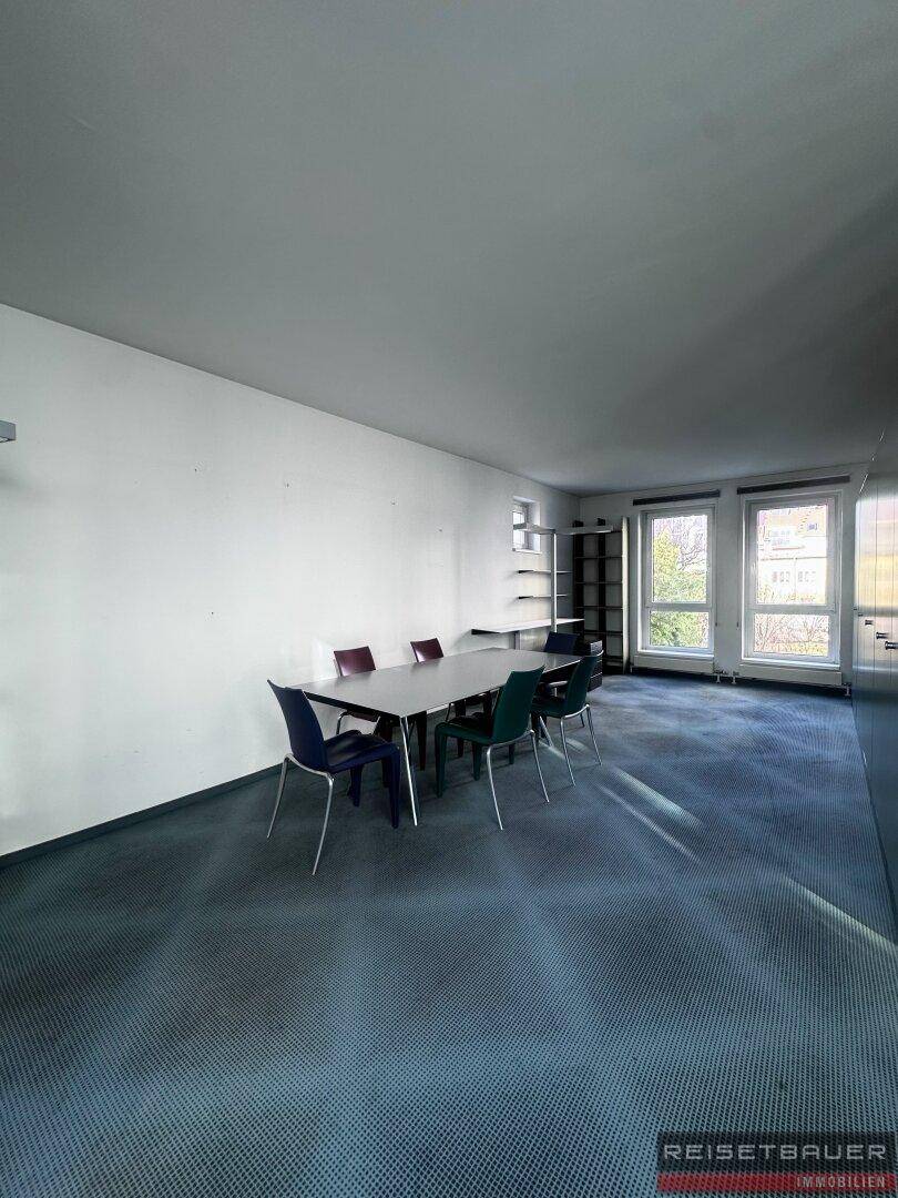 Geräumiges Büro mit Teppichboden, Besprechungstisch und großen Fenstern.