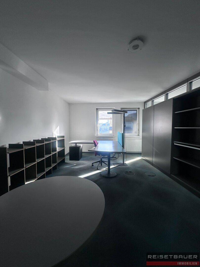 Geräumiges Büro mit Teppichboden, Regalen und einem runden Besprechungstisch.