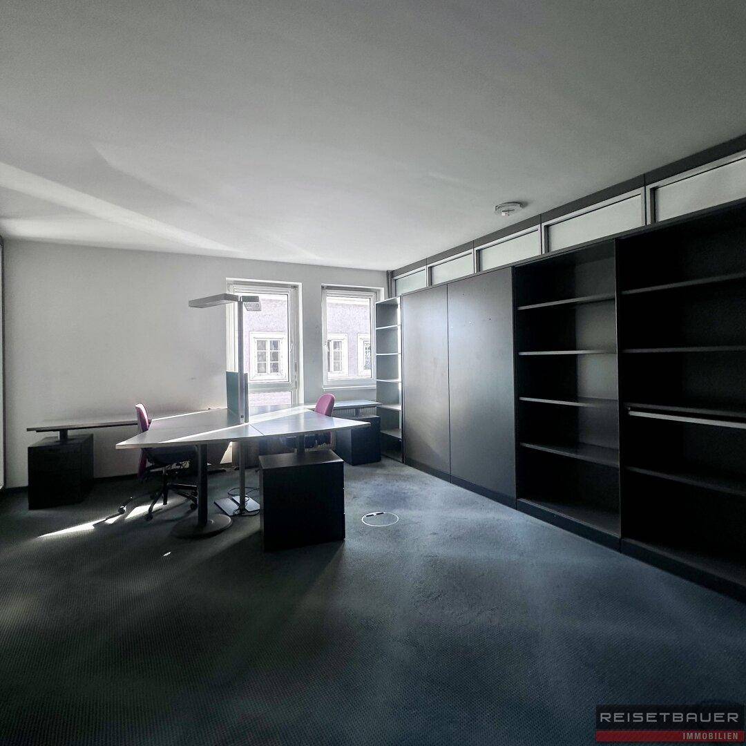 Helles Büro mit Teppichboden, Regalen und mehreren Arbeitsplätzen.