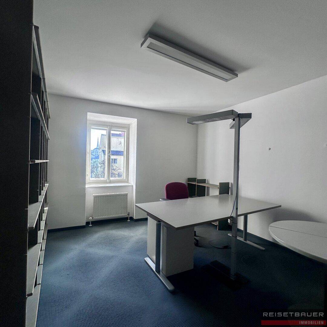 Geräumiges Büro mit Teppichboden, Regalen und einem Arbeitsplatz am Fenster.
