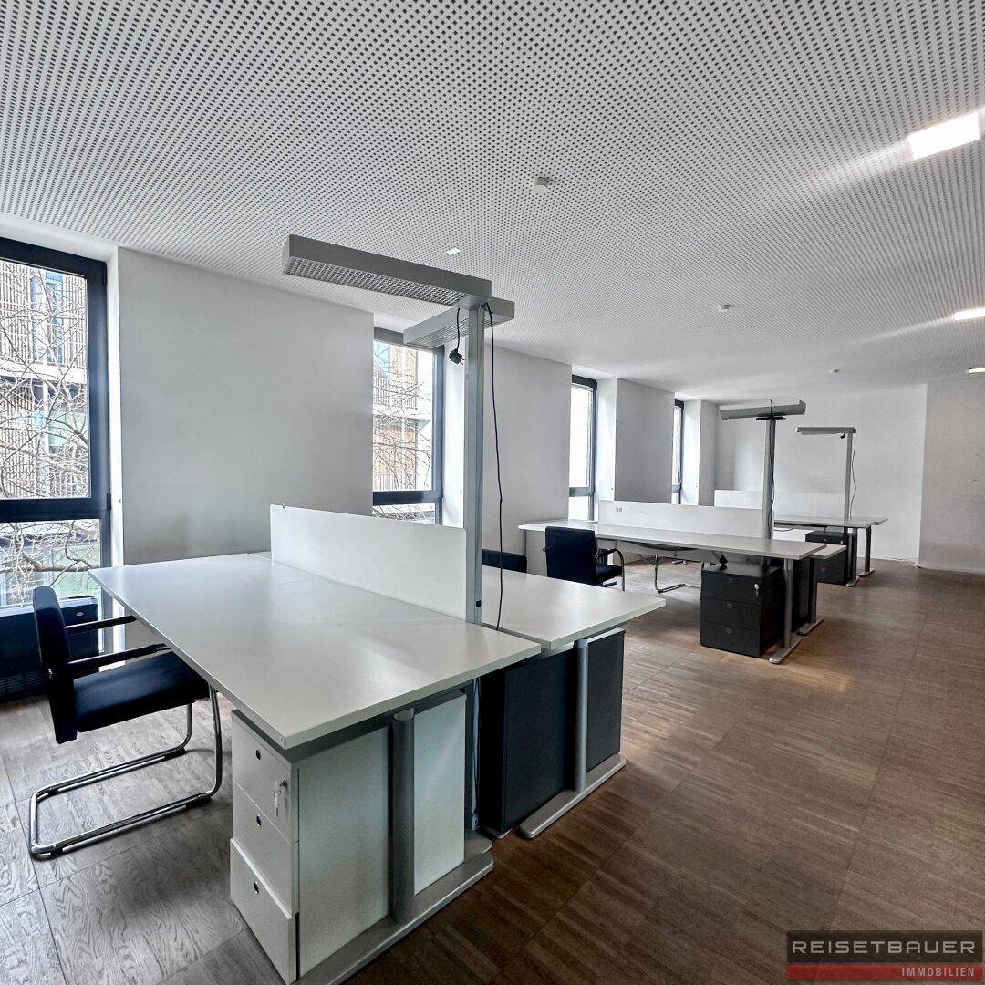 Helles und geräumiges Büro mit modernen Arbeitsplätzen, Trennwänden und großen Fenstern.