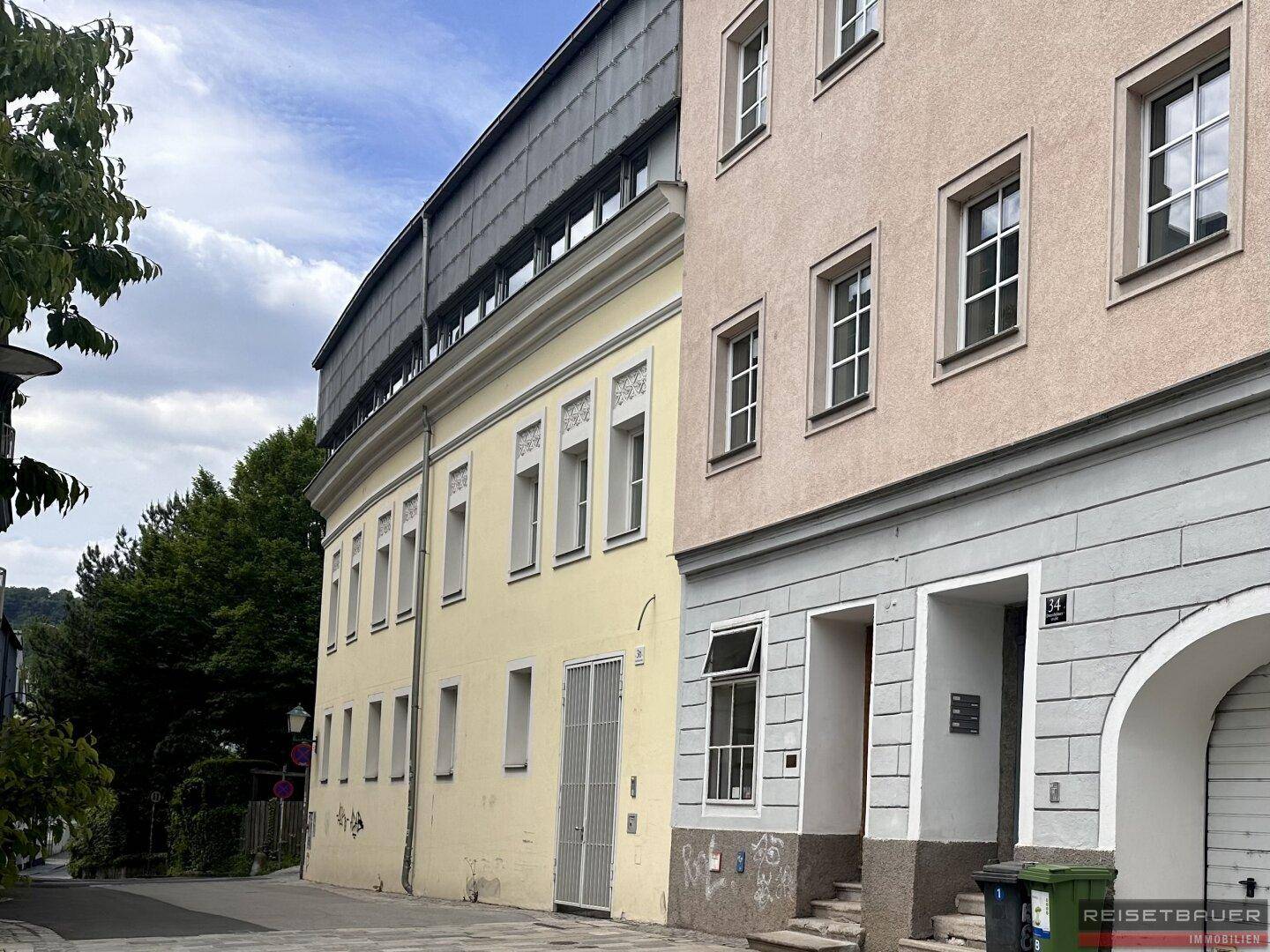 Ansicht von zwei Gebäuden an einer Straße mit traditioneller Architektur und modernen Elementen im oberen Bereich.