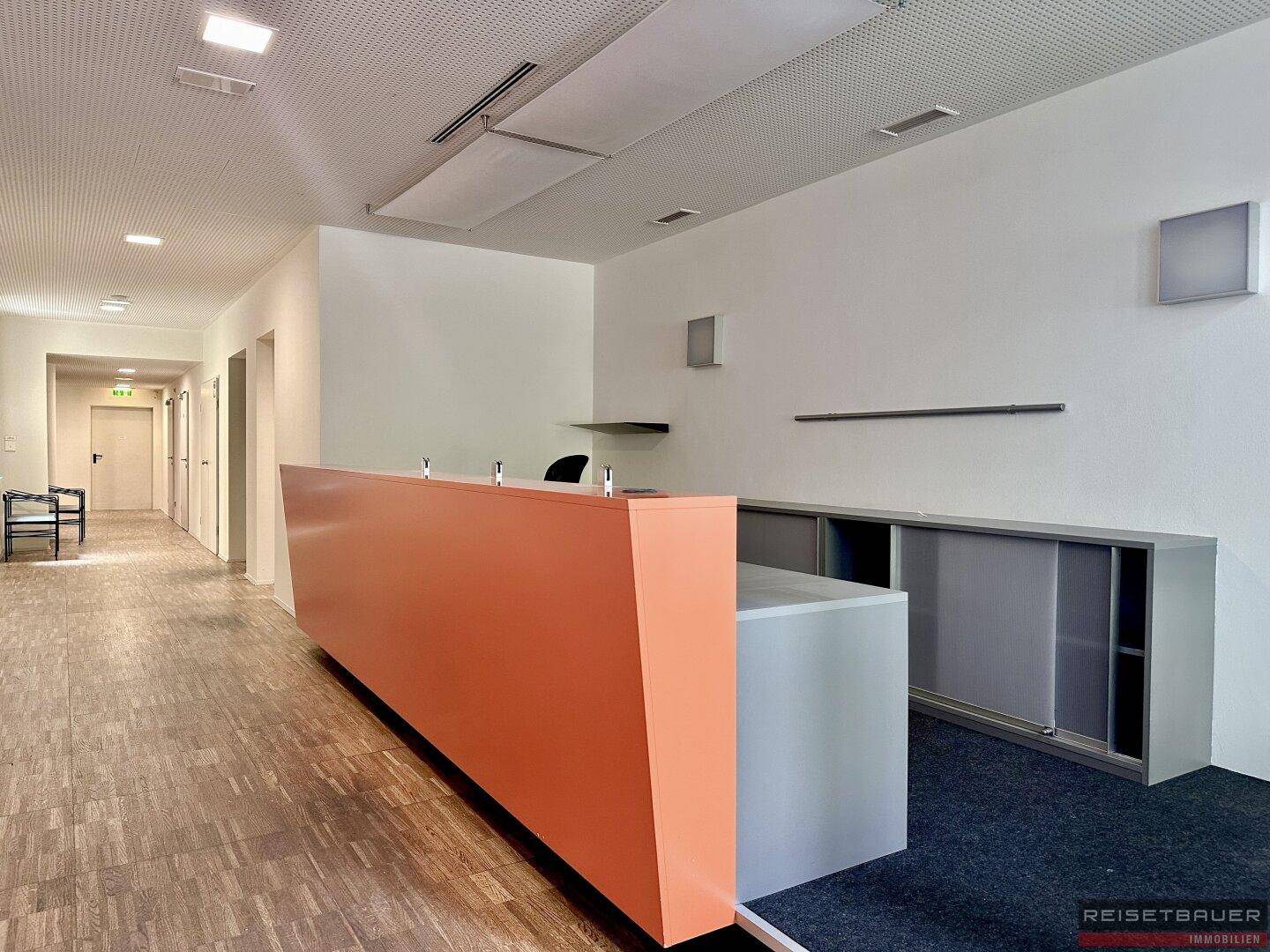 Empfangsbereich mit moderner Theke, Holzboden und Zugang zu weiteren Büros.