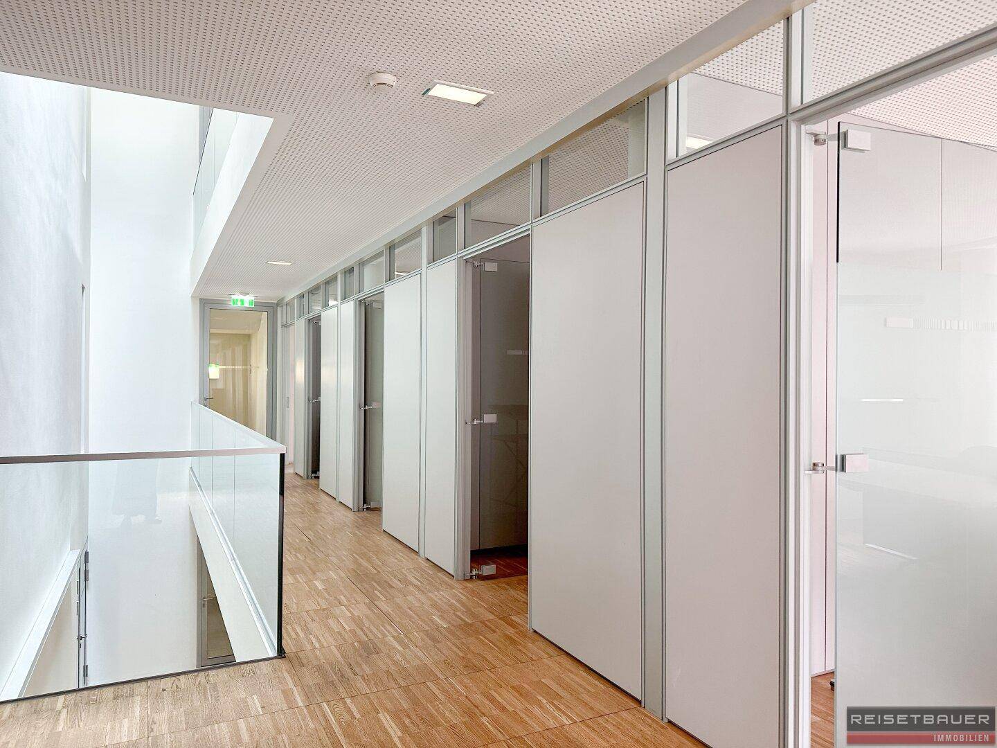 Heller Flur mit Glasgeländer, Holzfußboden und Büros mit Glaswänden auf einer Etage.