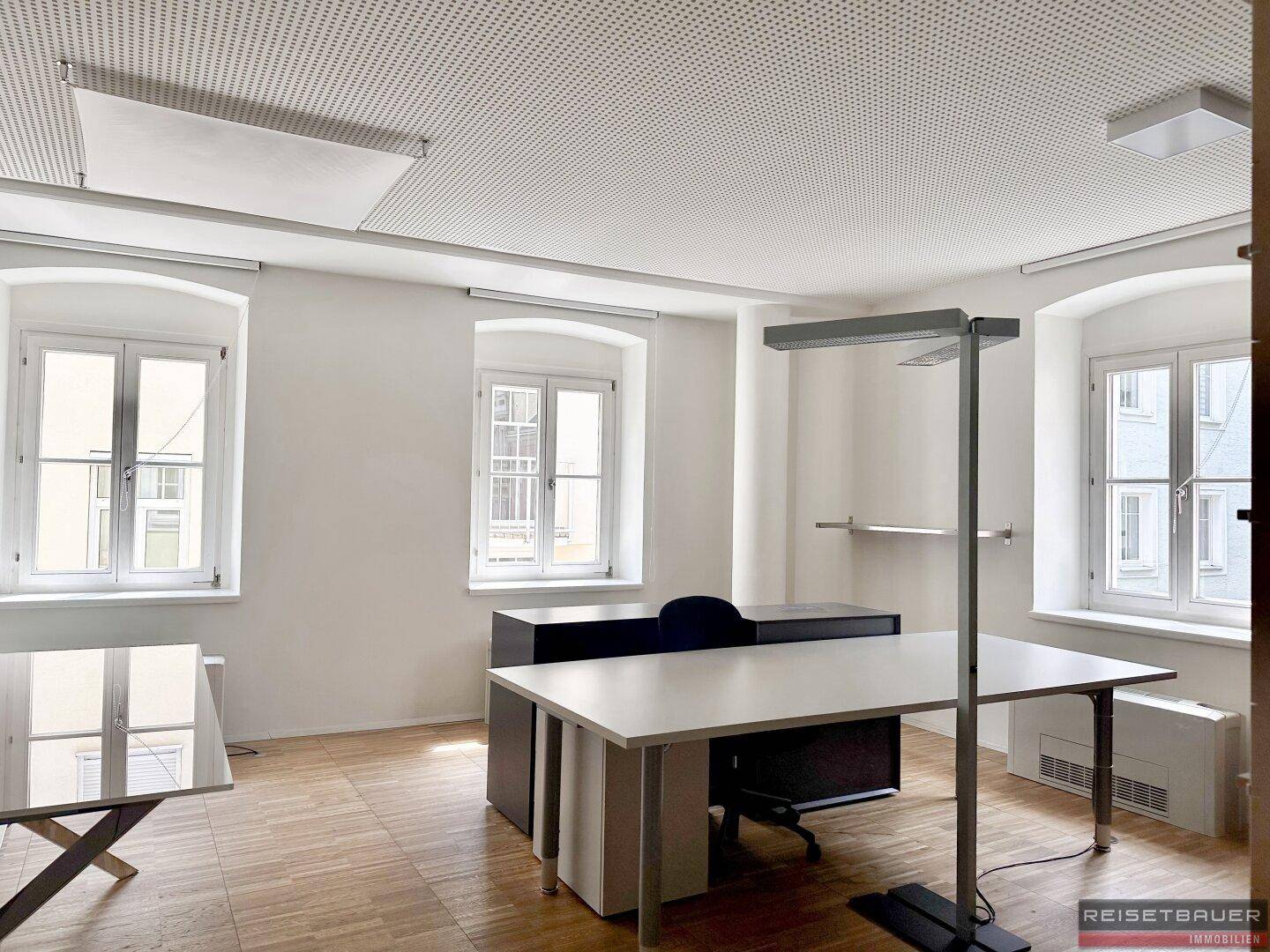 Geräumiges Büro mit mehreren Fenstern, Holzboden und modernen Büromöbeln.