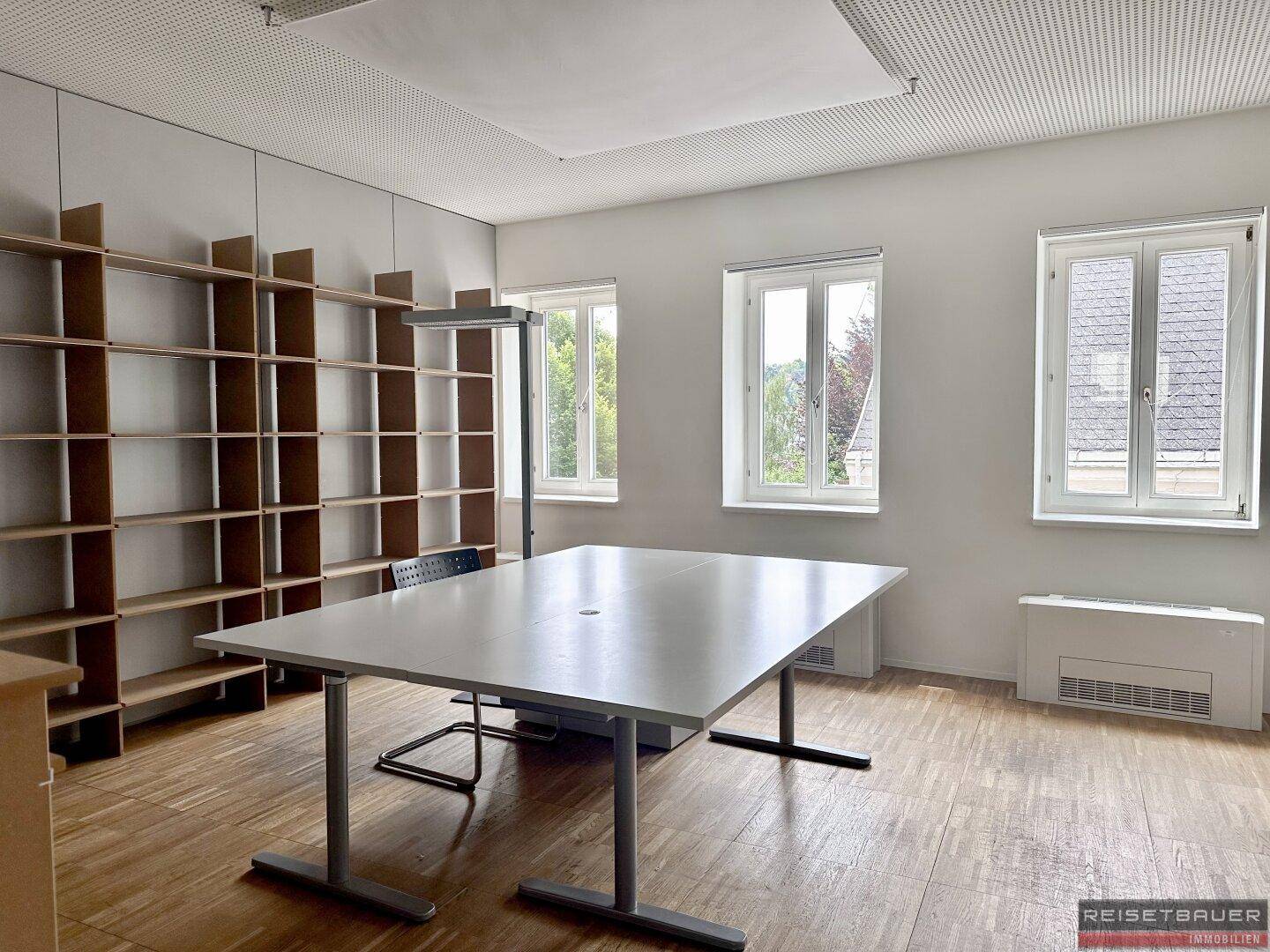Helles Büro mit Holzboden, Regalen und einem großen Tisch, ideal für Teamarbeit.