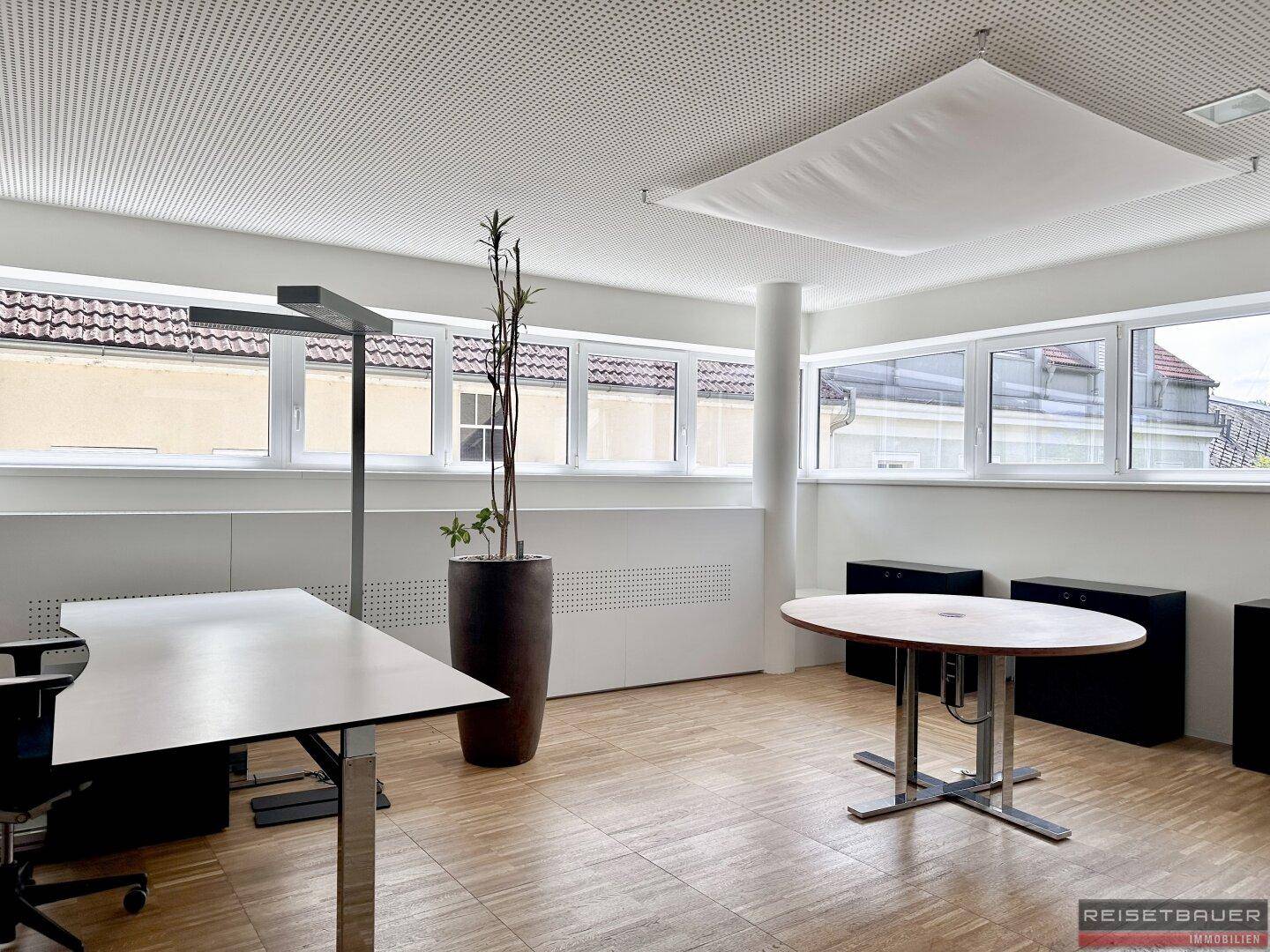 Helles Büro mit Holzboden, großen Fenstern und einem runden Besprechungstisch.