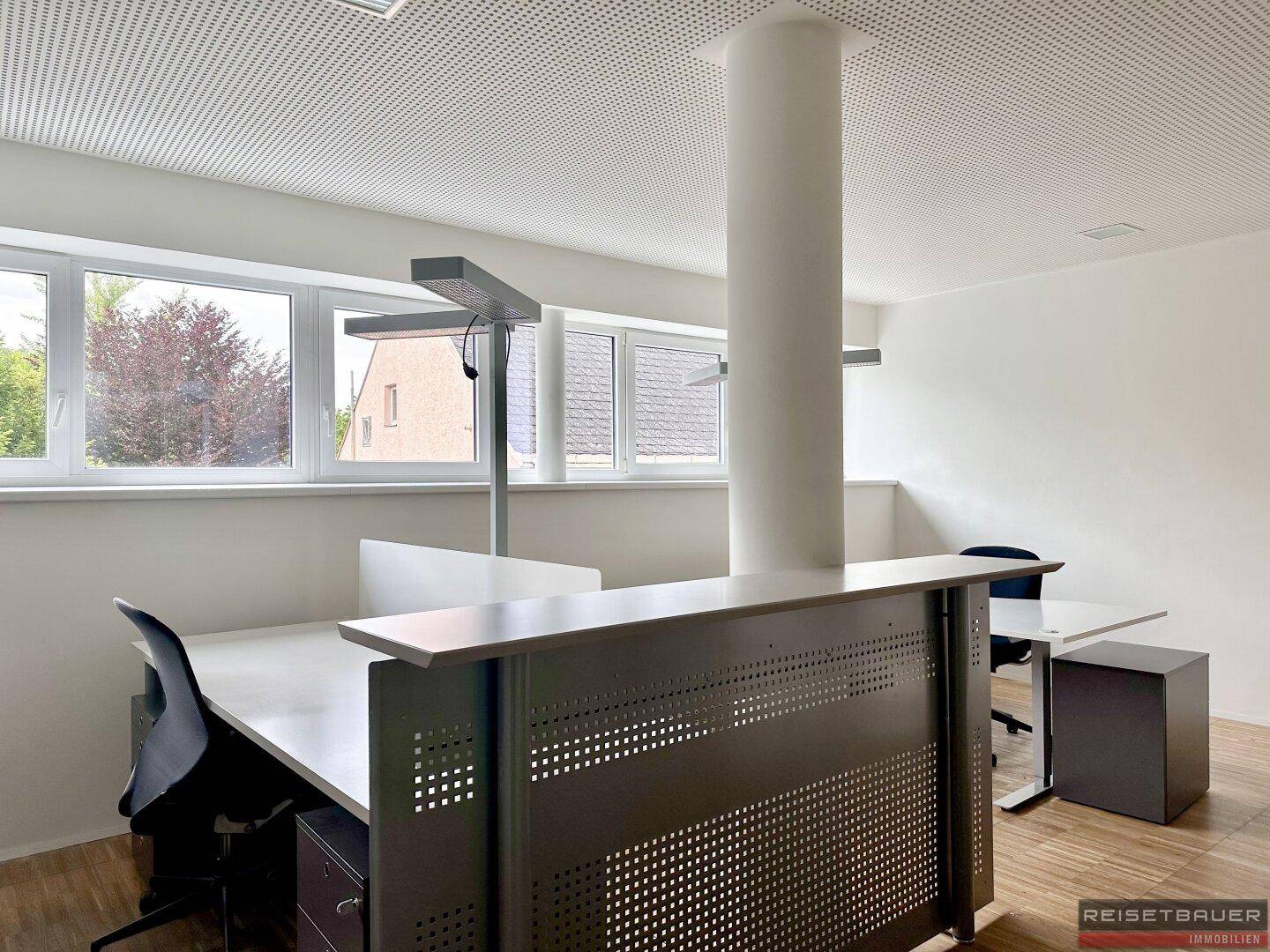 Offener Bürobereich mit mehreren Arbeitsplätzen, Holzboden und Säule in der Mitte.