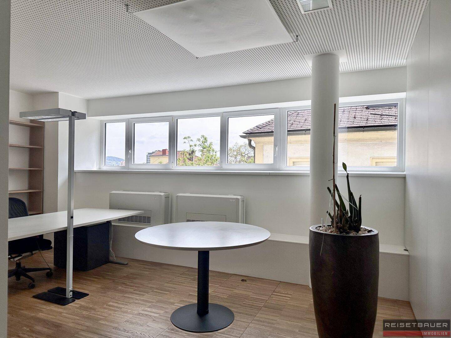 Helles Büro mit Holzboden, runden Tisch und großen Fenstern mit Ausblick.