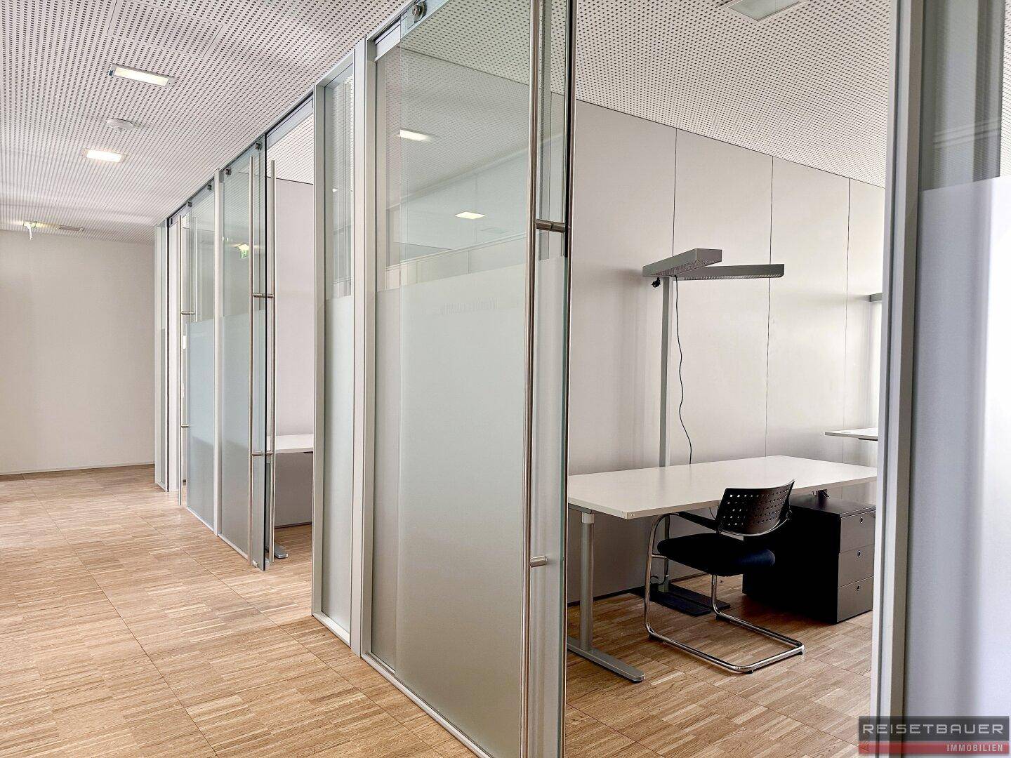 Bürobereich mit Glaswänden, Holzboden und einem Arbeitsplatz mit Schreibtisch und Stuhl.