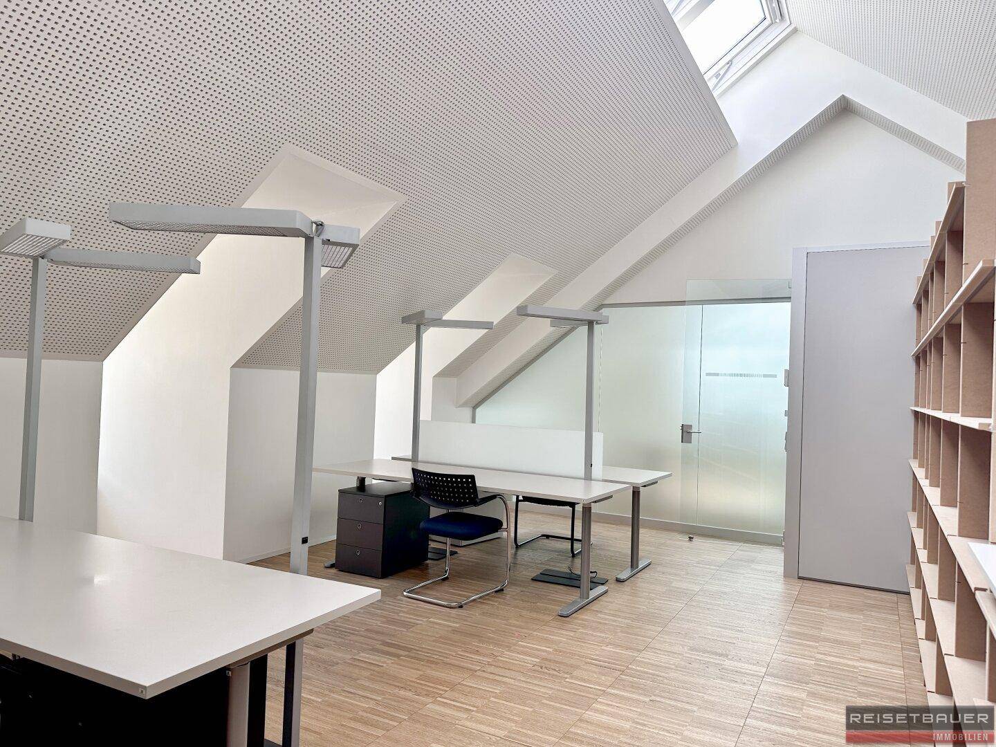 Dachgeschossbüro mit schrägen Wänden, Dachfenstern und mehreren Arbeitsplätzen.
