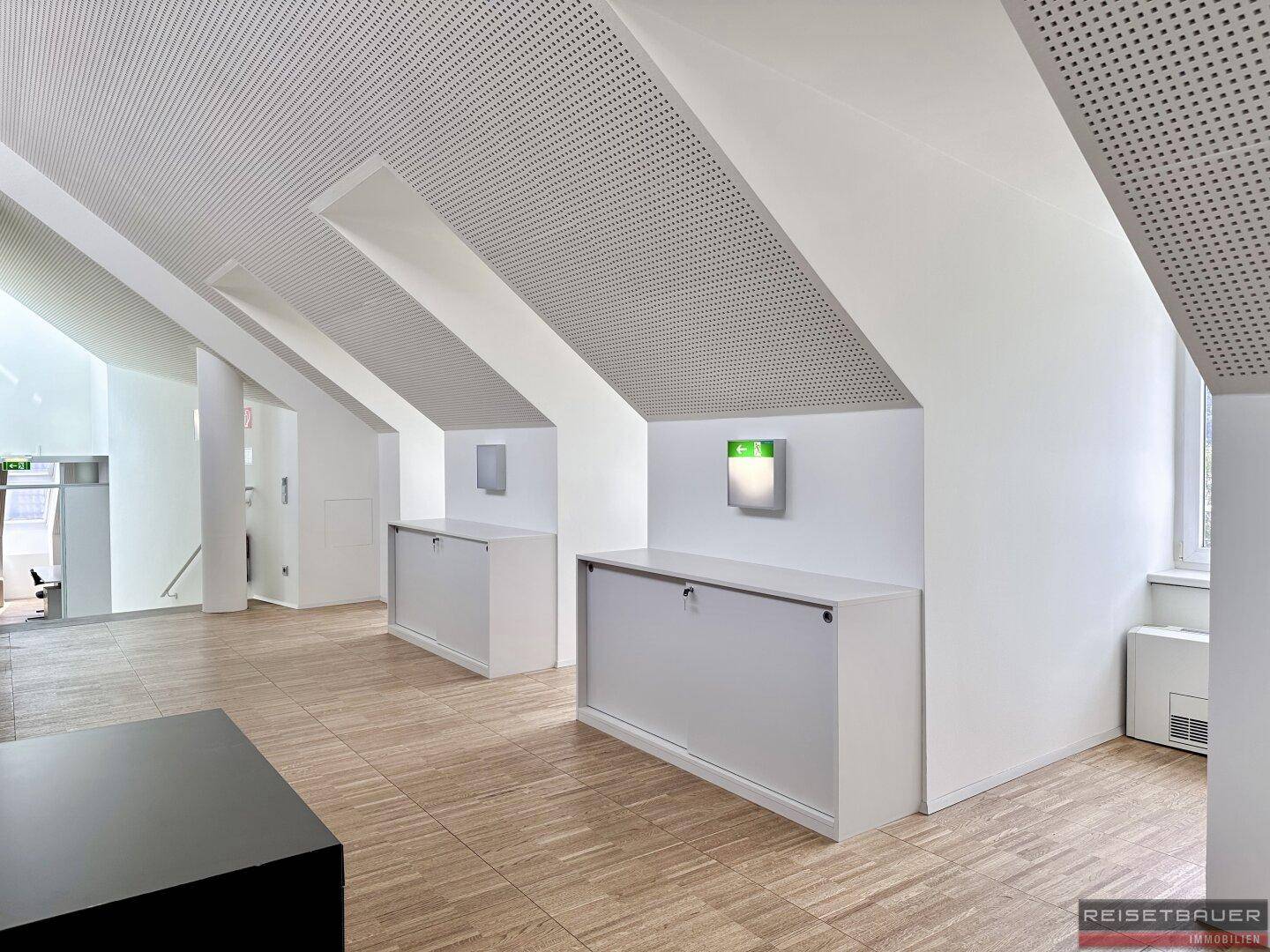 Dachgeschossbüro mit schrägen Wänden, Einbauschränken und Holzboden.