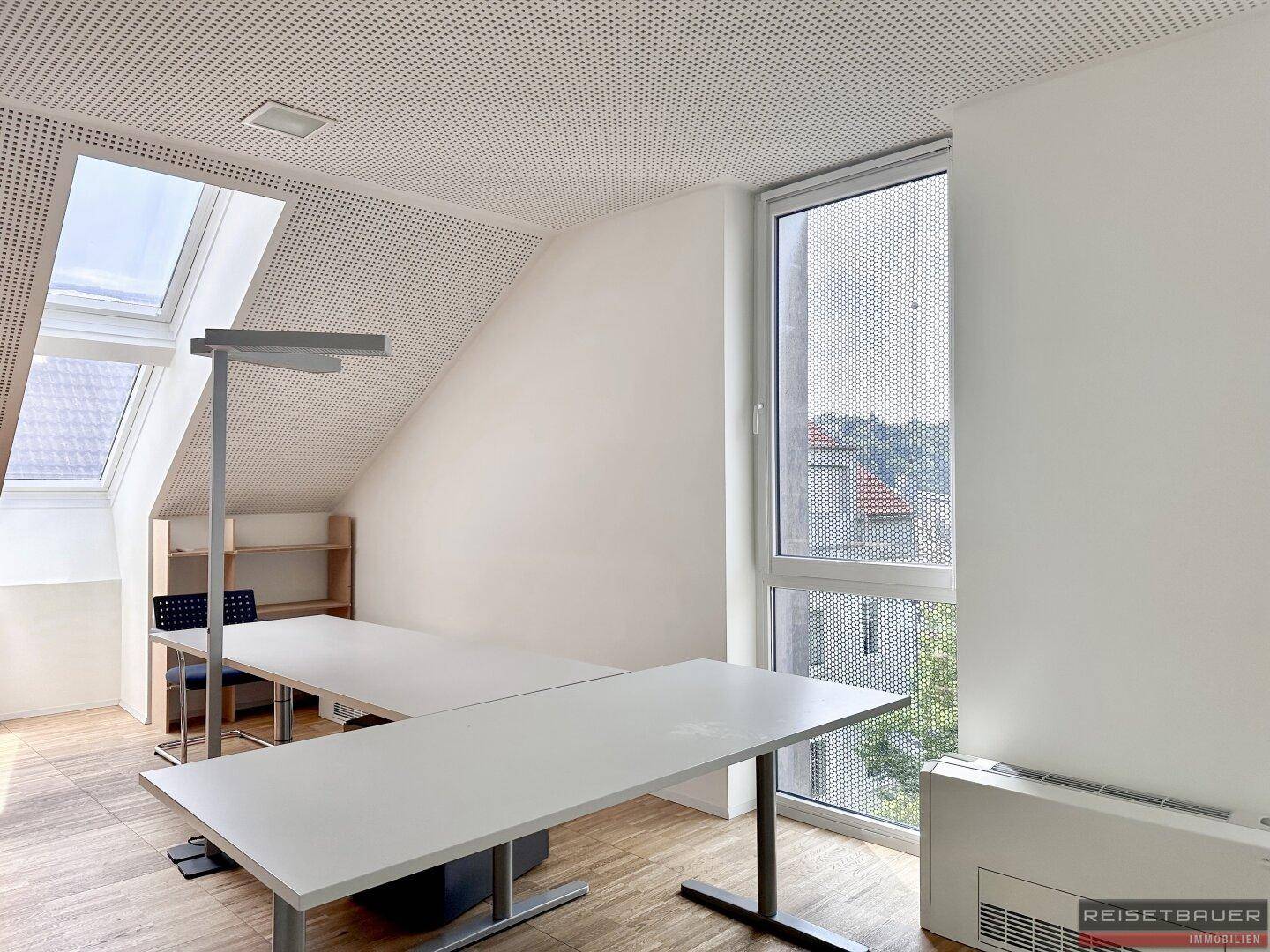 Dachgeschossbüro mit schrägen Wänden, Dachfenstern und einem großen Fenster mit Ausblick.