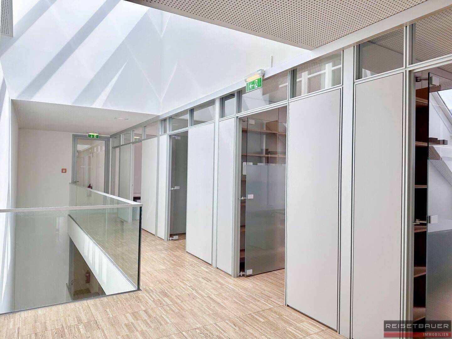 Heller Flur mit Glasgeländer, Holzfußboden und Büros mit Glaswänden auf einer Etage.