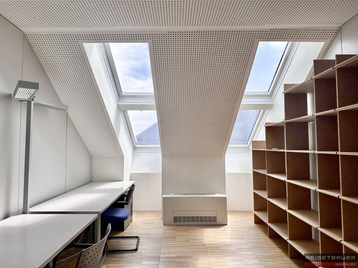 Dachgeschossbüro mit schrägen Wänden, mehreren Dachfenstern und Regalen.