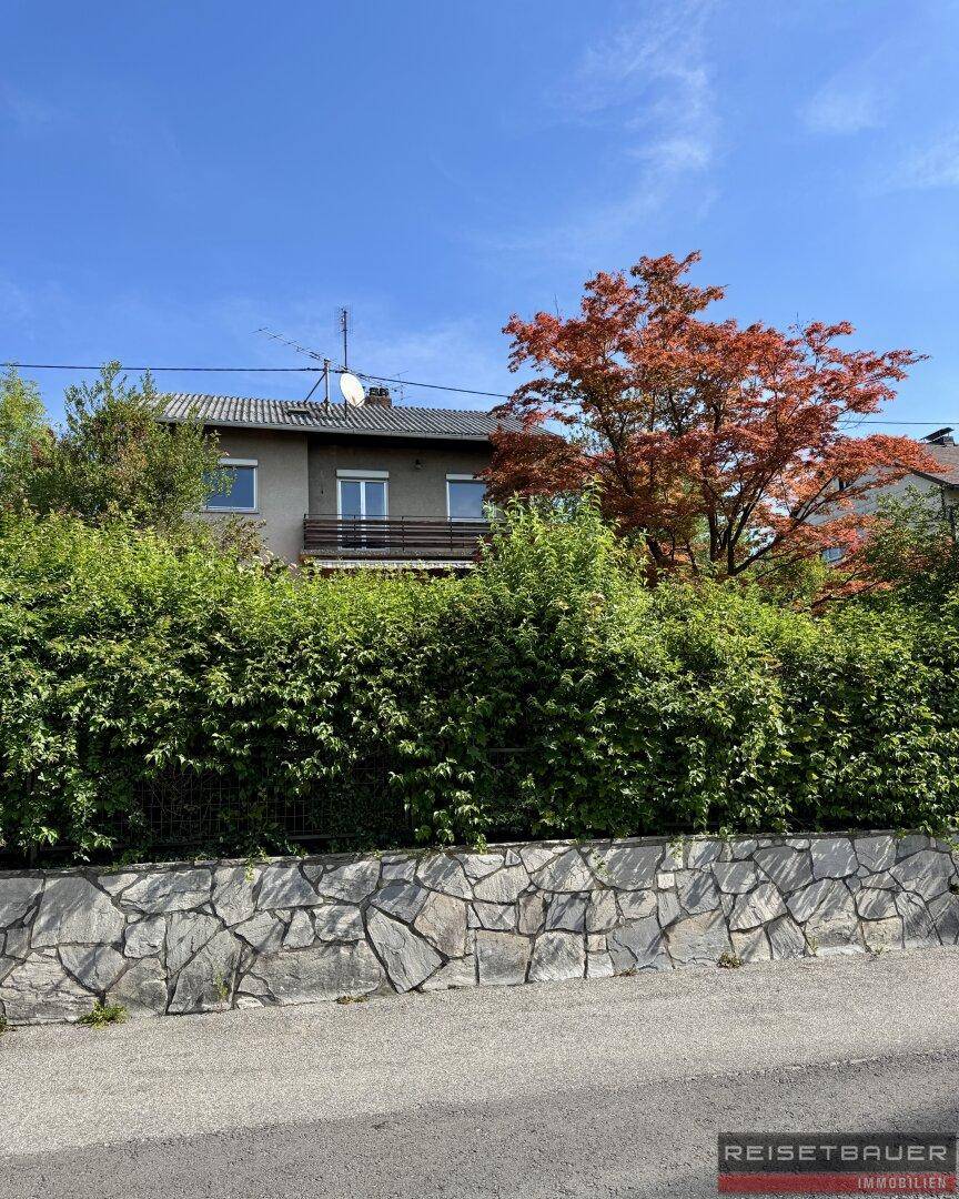 Ansicht des Hauses von der Straße, umgeben von einer Steinmauer und üppiger Heckenbepflanzung.