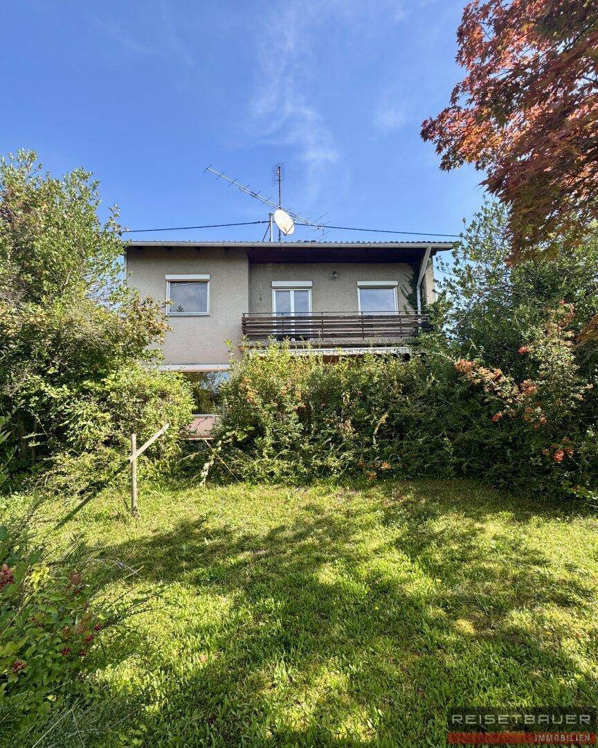 Rückseite des Hauses mit kleinem Balkon und einem weitläufigen, grünen Gartenbereich.