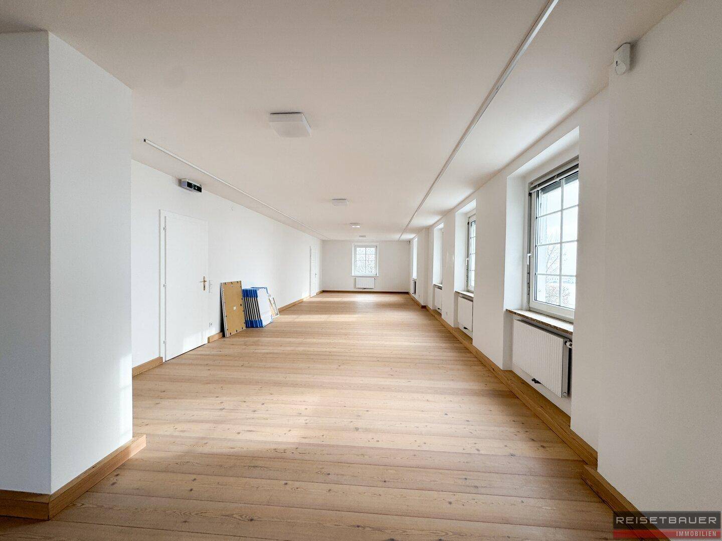 Langer, heller Bürogang mit vielen Fenstern und Holzboden, bietet viel Tageslicht.