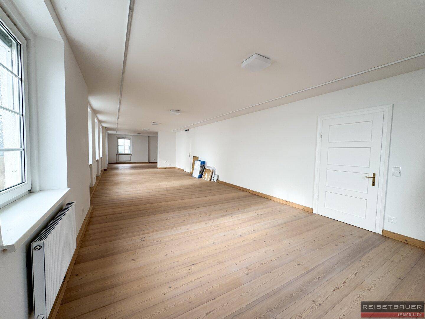 Heller Büroraum mit Holzboden und großen Fenstern, bietet eine angenehme Arbeitsatmosphäre.
