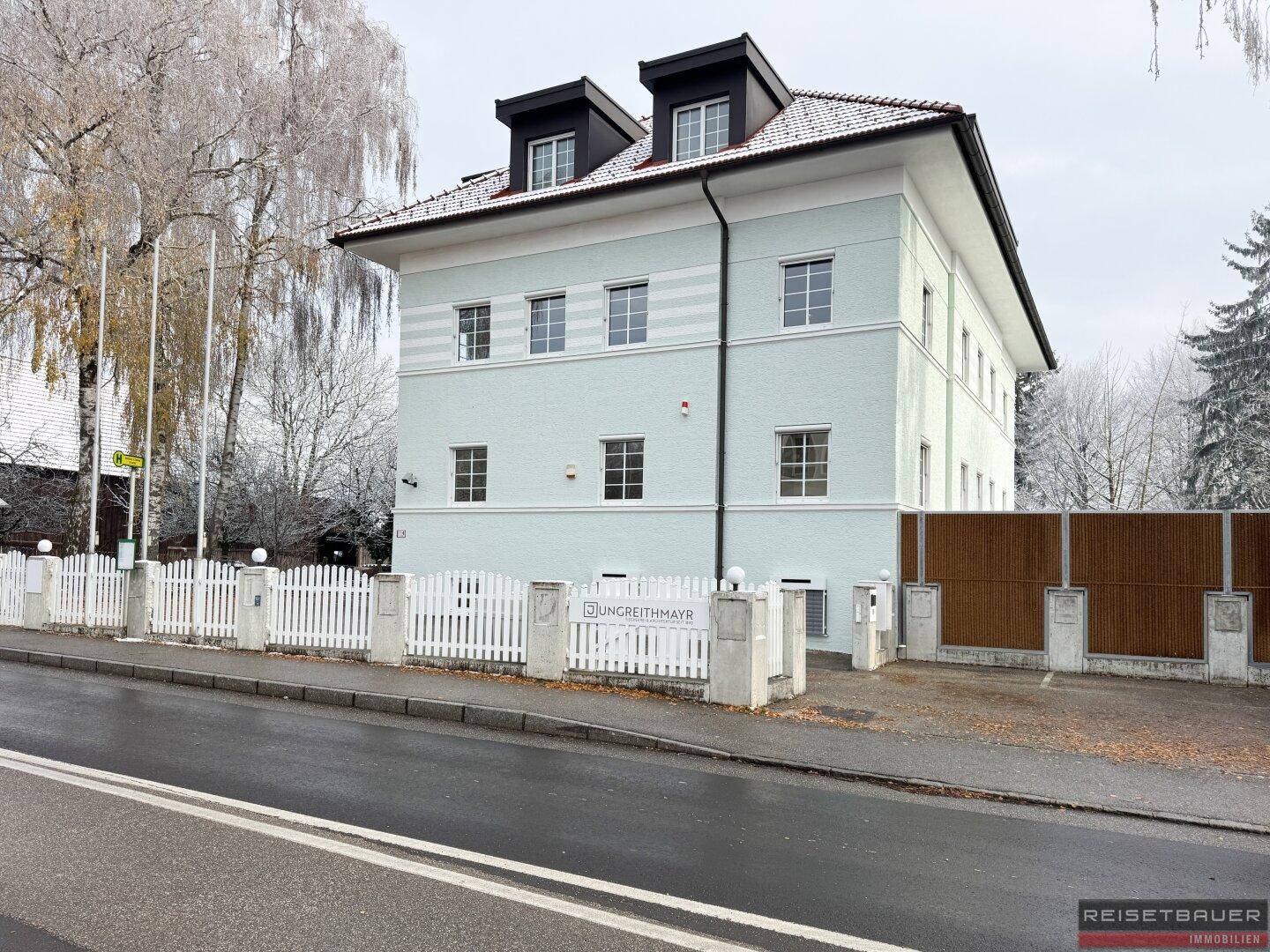 Attraktives Gebäude mit heller Fassade und Dachgauben, umgeben von winterlicher Vegetation.