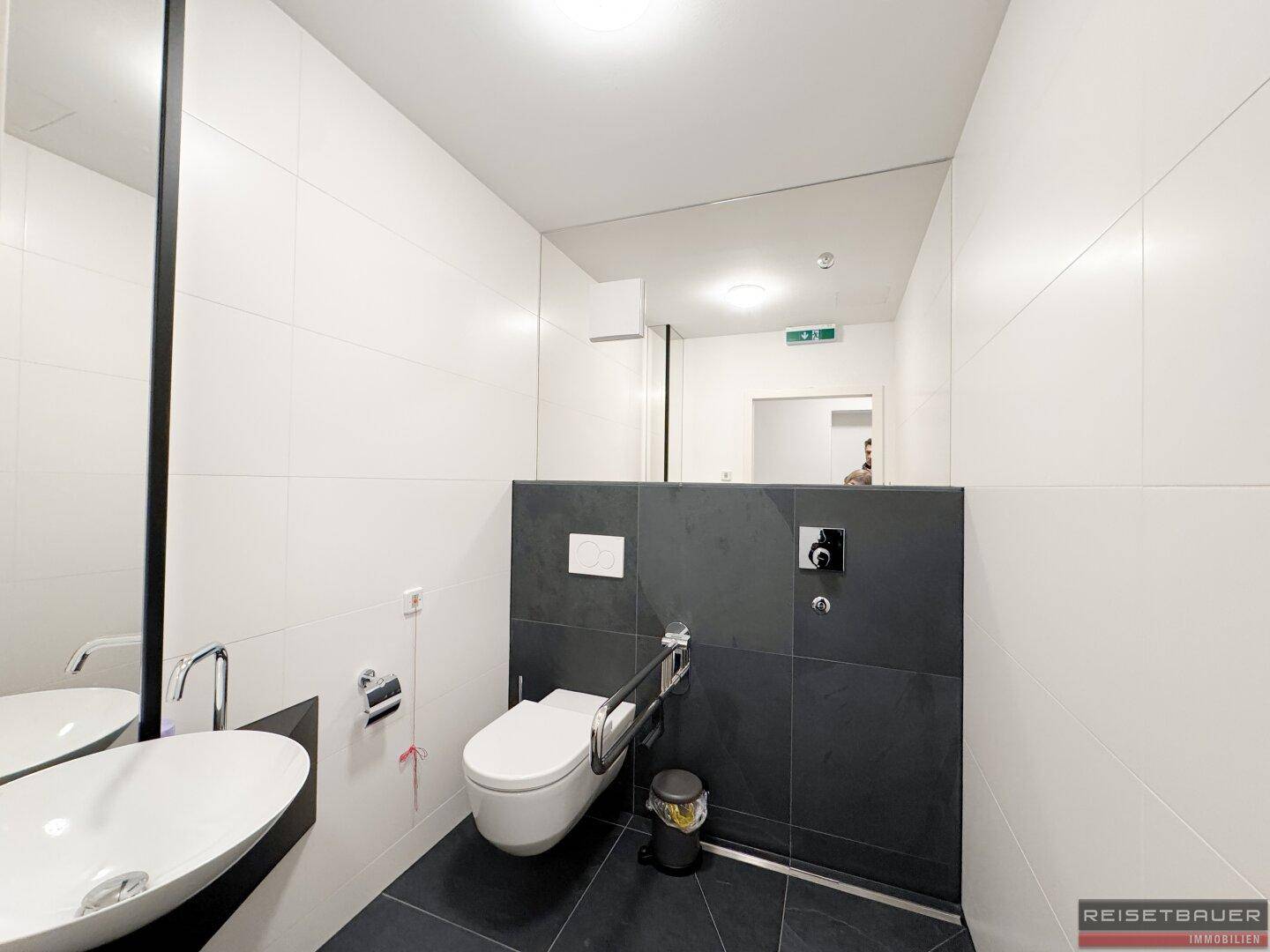 Barrierefreies Badezimmer mit Haltegriffen, wandhängender Toilette und modernem Waschbecken.