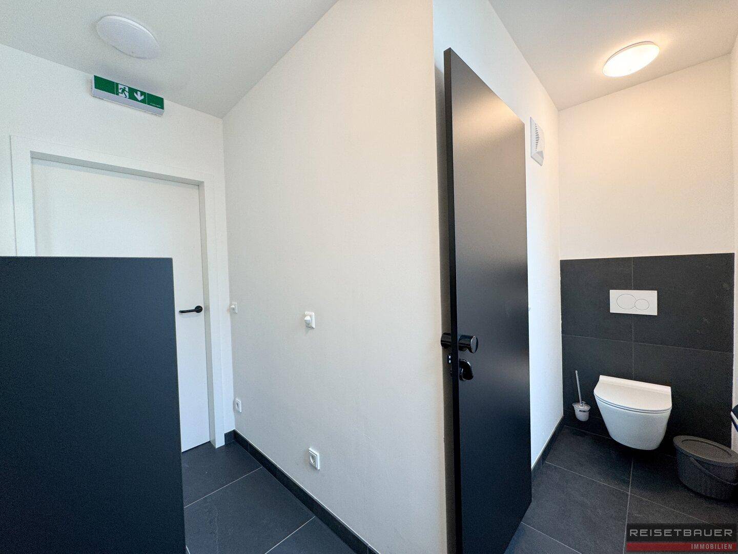 Modernes WC mit dunklen Fliesen und wandhängender Toilette, sauber und funktional.