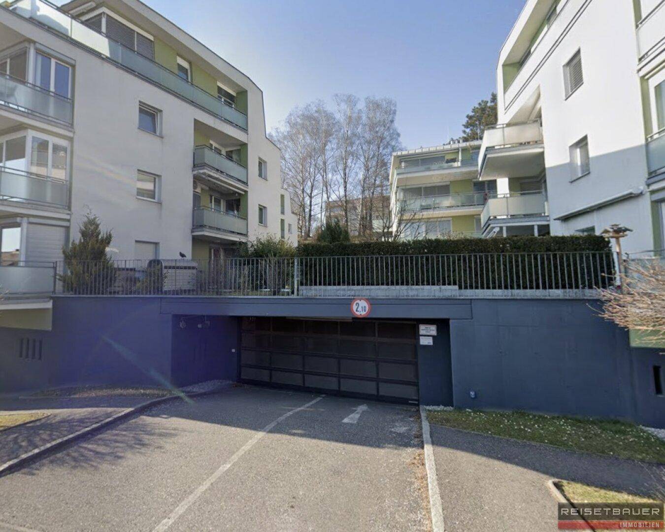 Einfahrt zur Tiefgarage eines modernen Wohnkomplexes mit mehreren Gebäuden und Balkonen.