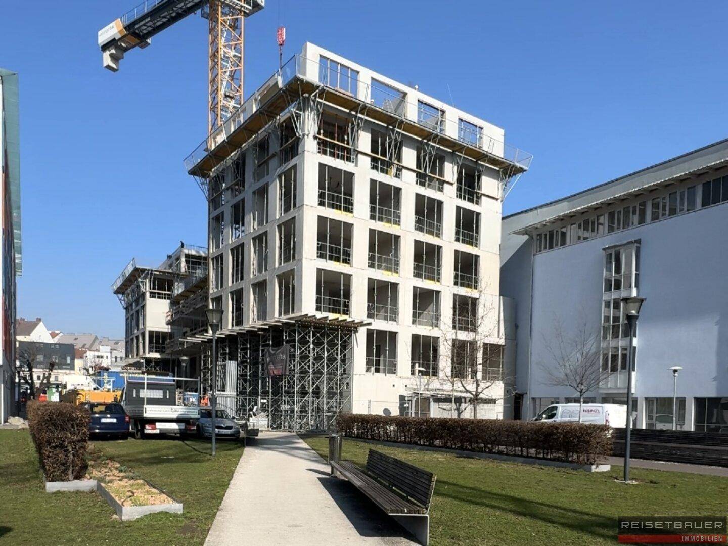 Modernes Wohngebäude im Bau mit sichtbaren Gerüsten und einem Baukran unter blauem Himmel.