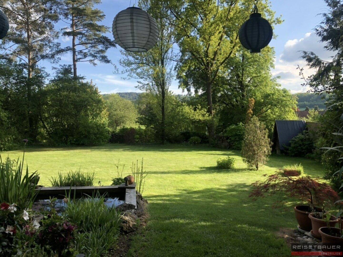 Großer, gepflegter Garten mit Rasenfläche, Bäumen und einem kleinen Teich.