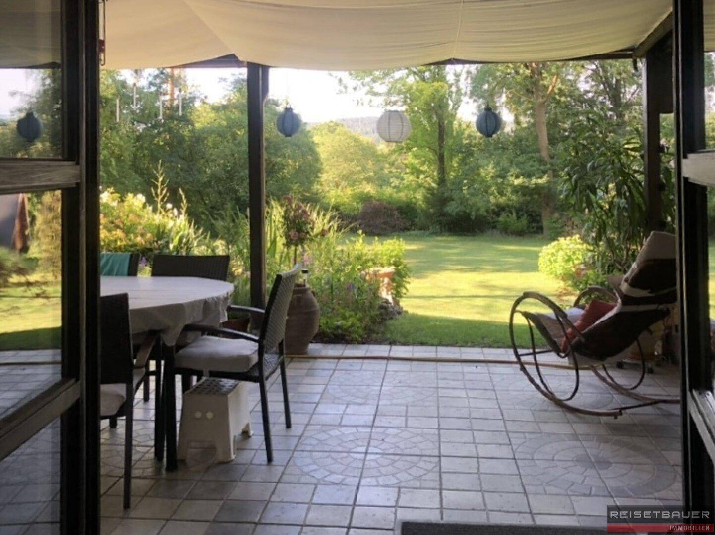Überdachte Terrasse mit Fliesenboden und Gartenmöbeln, mit Blick auf den grünen Garten.