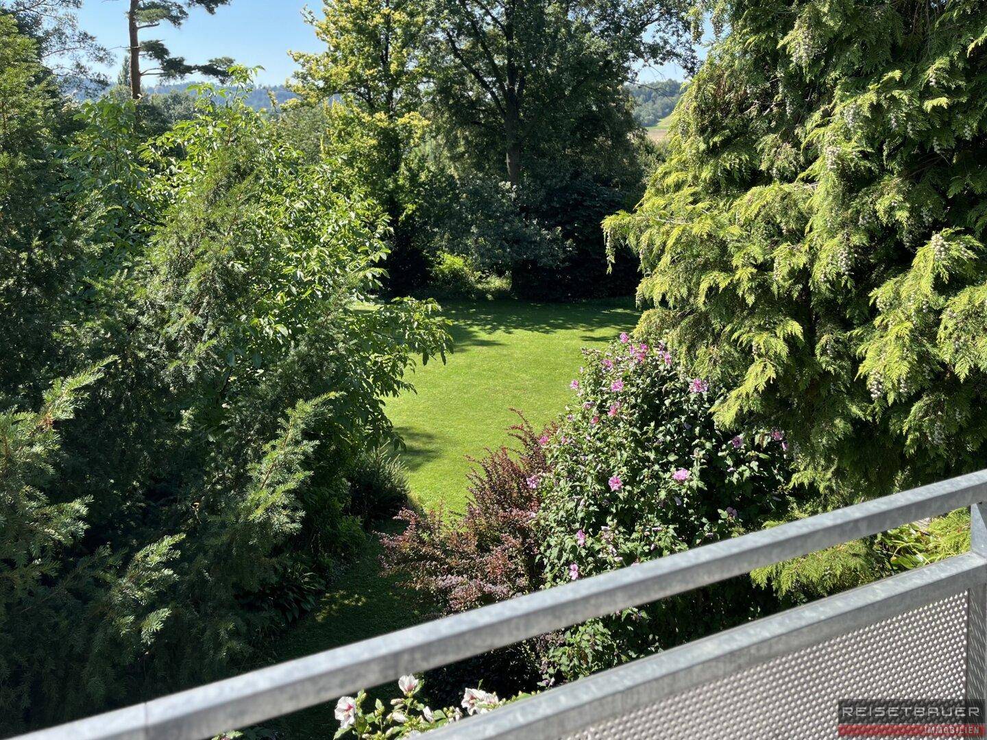 Blick von einem Balkon auf den weitläufigen, grünen Garten mit Bäumen und Sträuchern.