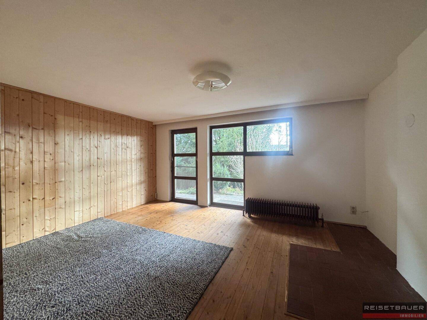 Geräumiges Zimmer mit Holzboden, Holzvertäfelung und Zugang zum Außenbereich.