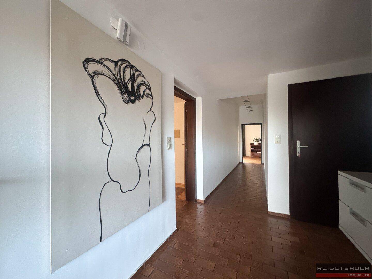 Langer Flur mit Fliesenboden und moderner Kunst an der Wand, der zu weiteren Räumen führt.
