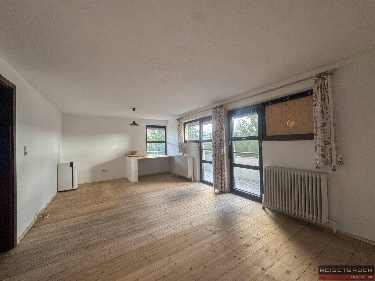 Geräumiges Wohnzimmer mit Holzboden und Zugang zu einem Balkon, hell und einladend.