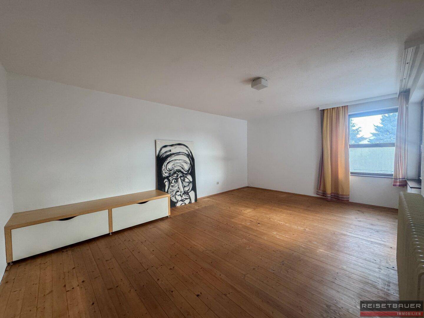 Helles Schlafzimmer mit Holzboden und einem großen Fenster, das viel Licht spendet.