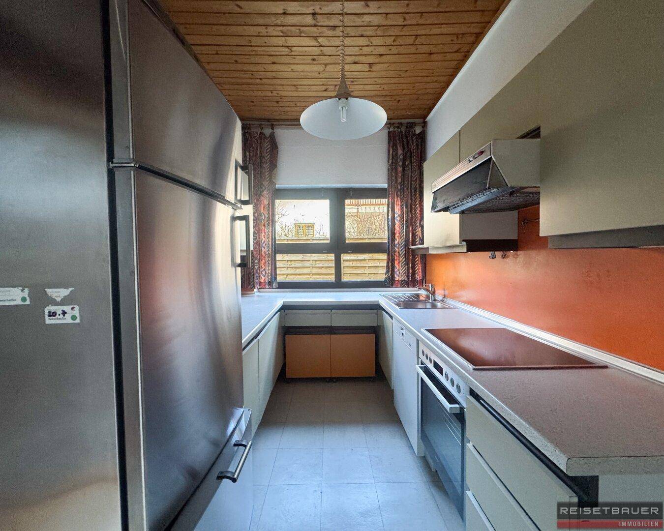 Schmale Küche mit Fliesenboden, Einbauküche und Fenster, das Tageslicht spendet.