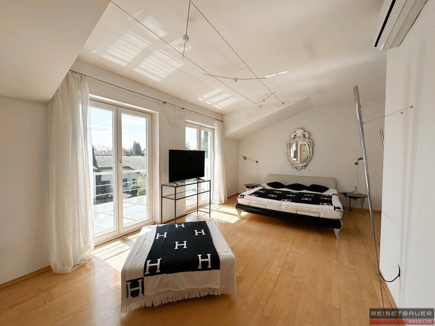 Helles Schlafzimmer mit Holzboden, Dachschräge und großen Fenstertüren, die viel Licht spenden.