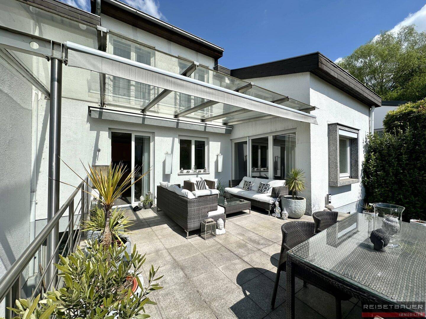 Großzügige, möblierte Terrasse mit Outdoor-Lounge-Möbeln und einer transparenten Überdachung.